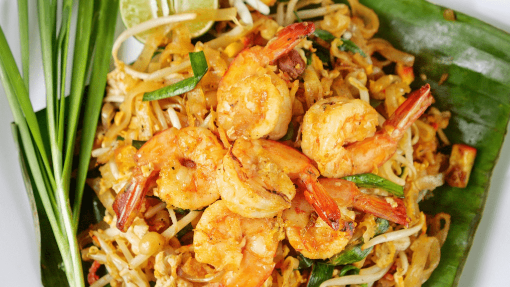 a plate of pad thai with shrimp, green beans and cashews