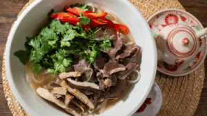 a bowl of beef noodle soup with chopsticks on a wooden table