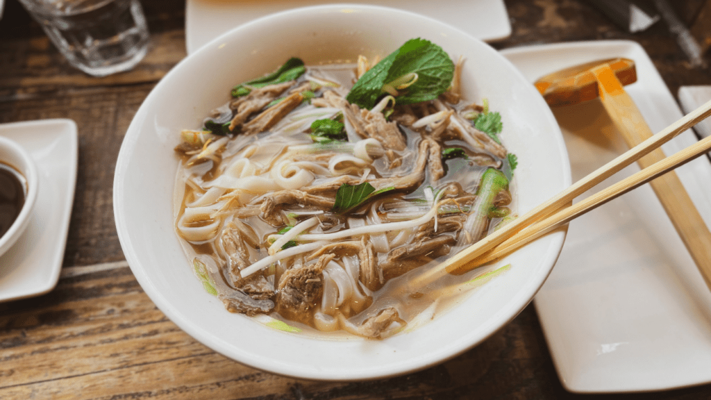 a bowl of beef noodle soup with chopsticks on a wooden table