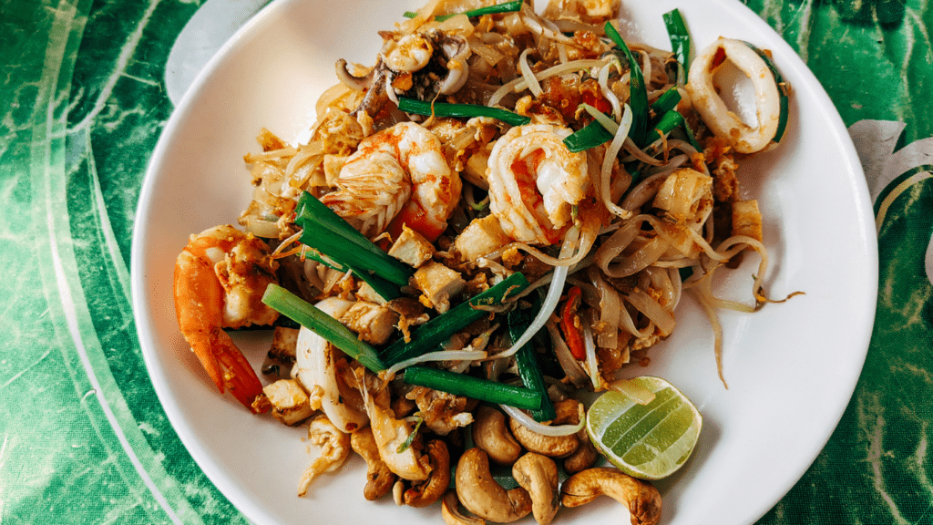 a plate of pad thai with shrimp, green beans and cashews